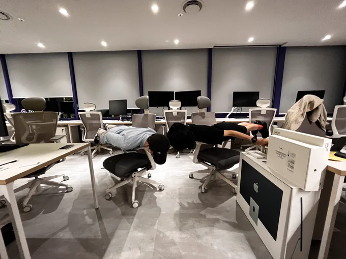 Photo of two people lying horizontally across chair armrests, experiencing (physically) horizontal work culture